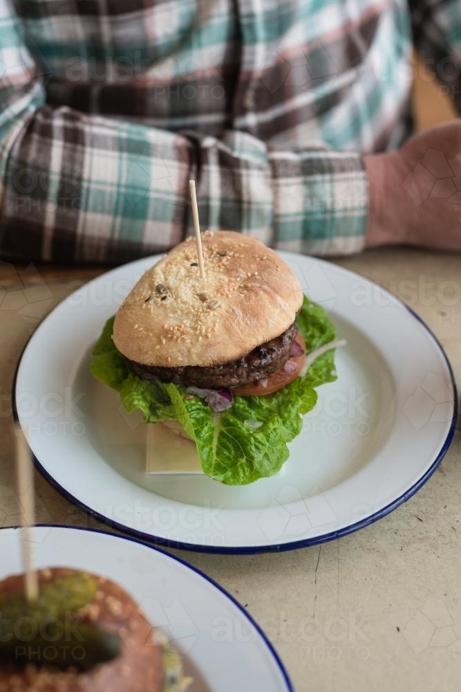 gourmet hamburger, indoors with man in checked shirt at table - Australian Stock Image