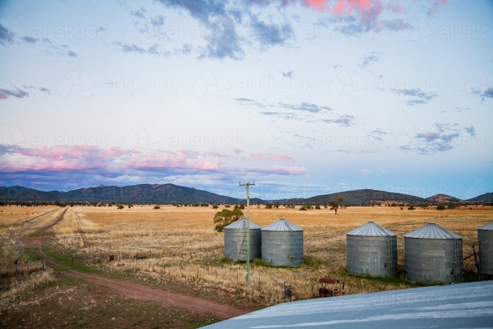 Grain silos on a farm at dusk with pink clouds - Australian Stock Image