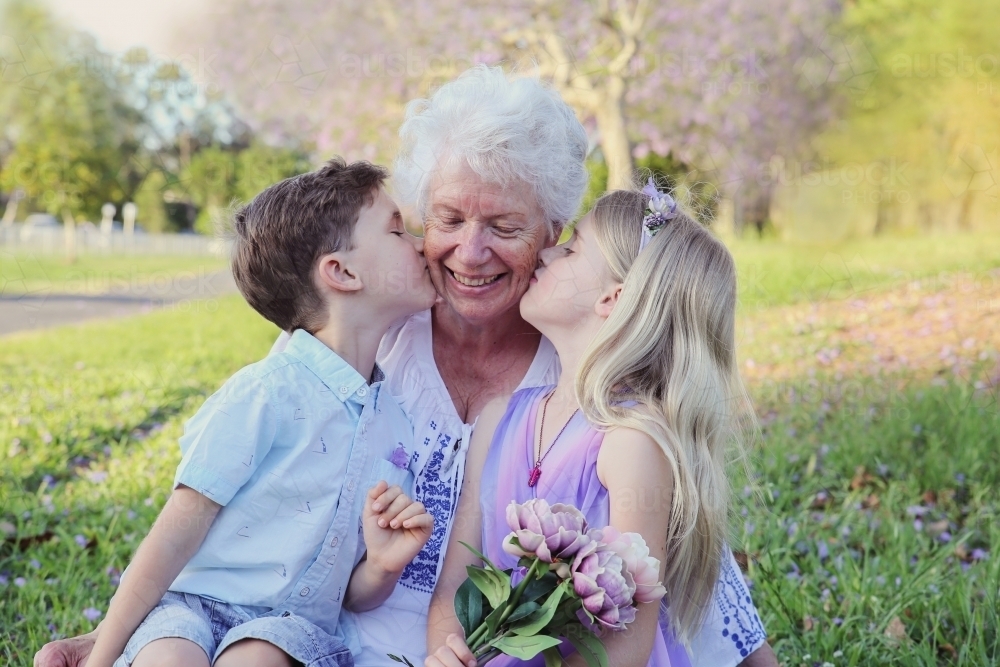 Grandchildren kissing their grandmother in the park - Australian Stock Image