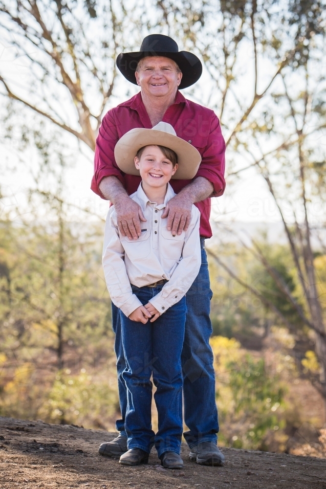Grandfather standing with hands on shoulders of grandson on farm in drought - Australian Stock Image