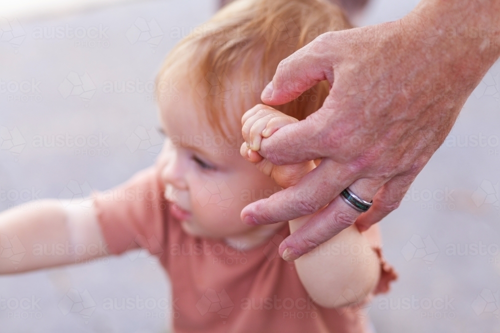 Grandfathers hand holding baby's hand helping baby to walk - Australian Stock Image