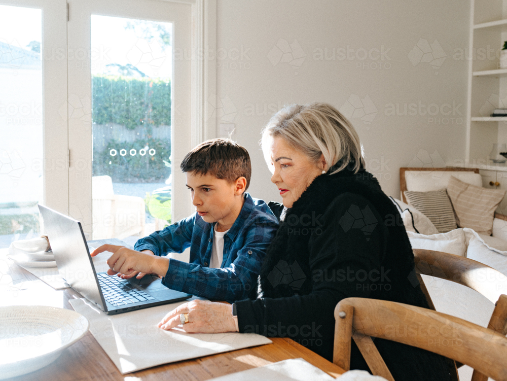 Grandma sitting with her grandson in front of a laptop on the table. - Australian Stock Image