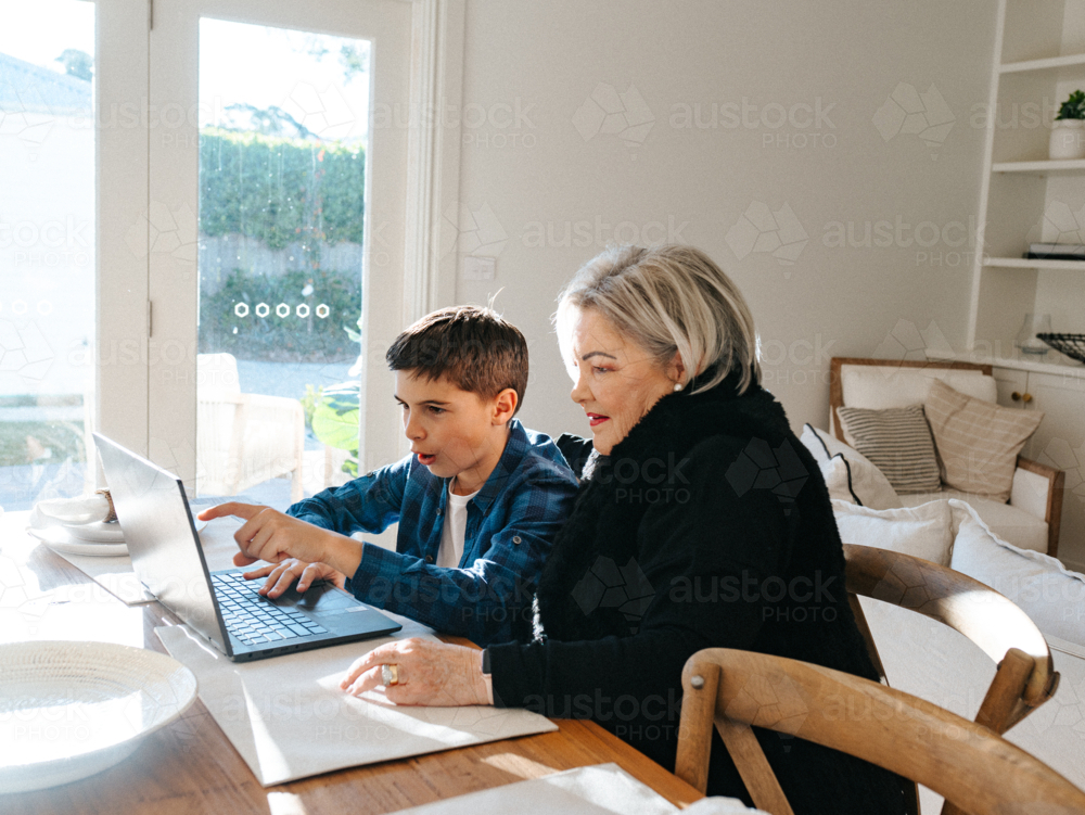 Grandma sitting with her grandson in front of a laptop on the table. - Australian Stock Image