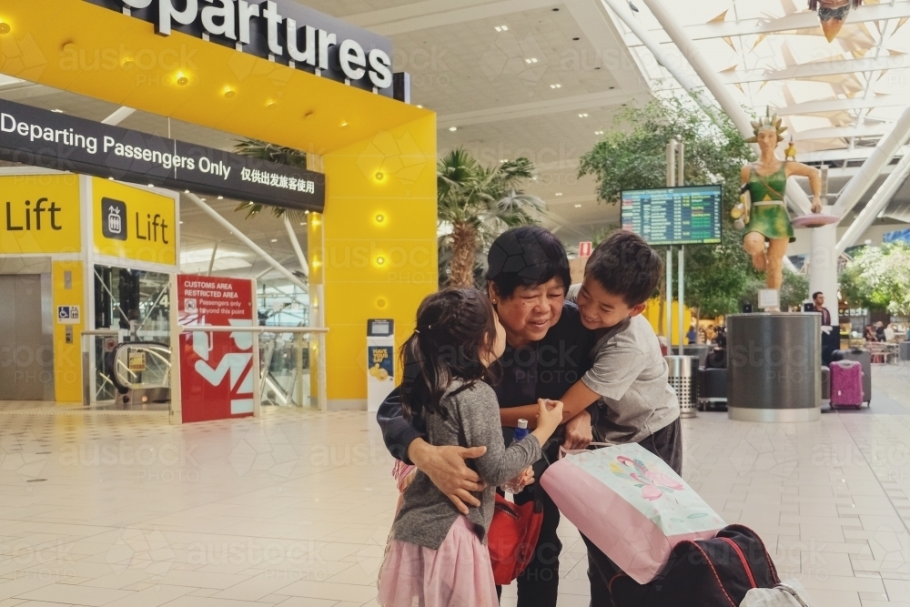 Grandmother and grandchildren hugging and saying goodbye at departures gate at an airport - Australian Stock Image