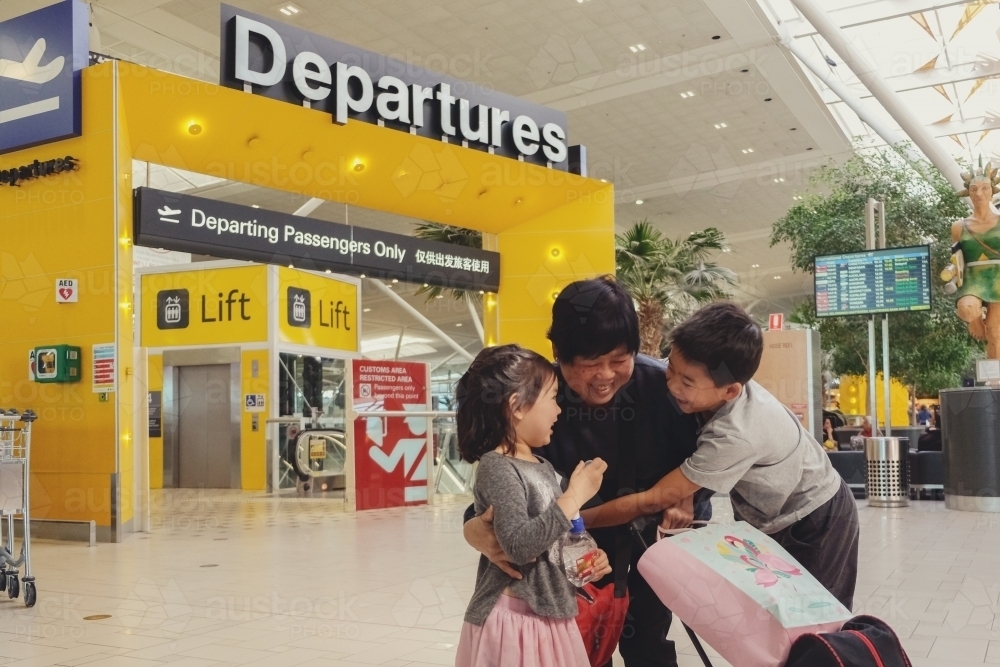 Grandmother and grandchildren hugging and saying goodbye at departures gate at an airport - Australian Stock Image