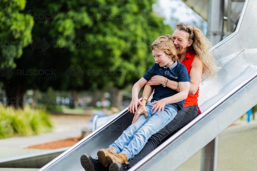 grandmother and grandson going down slide at playground - Australian Stock Image