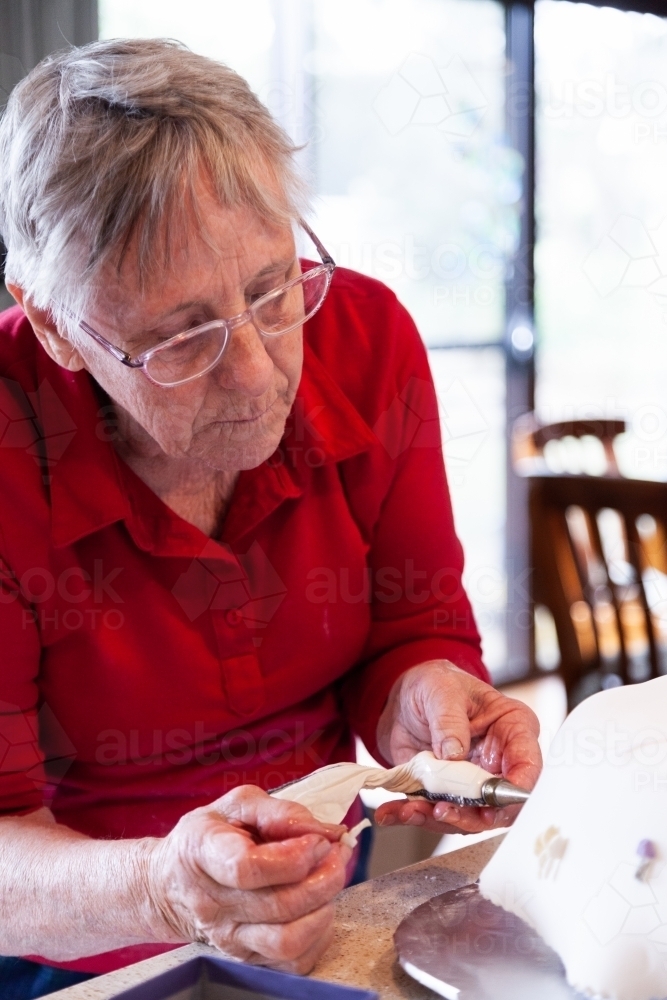 Grandmother piping icing onto fancy cake - Australian Stock Image