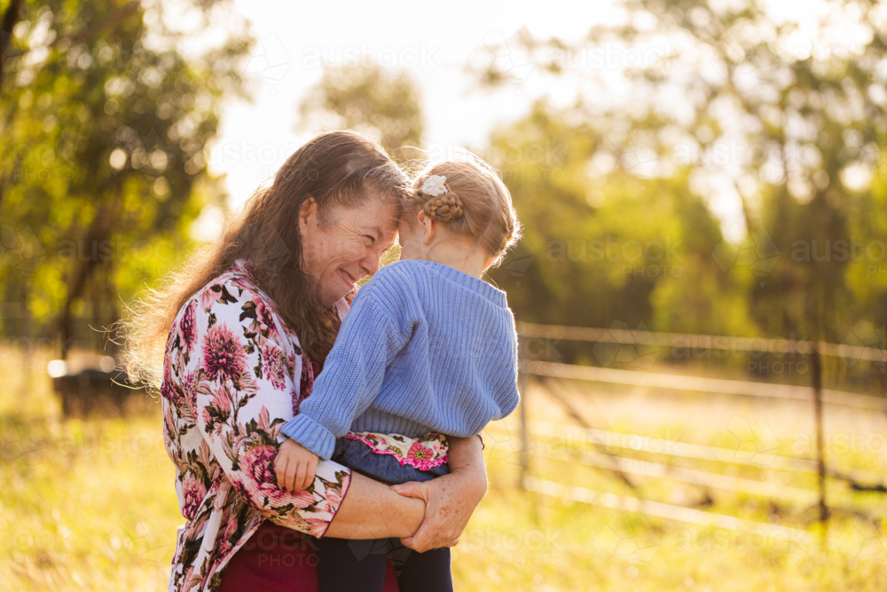 grandmother smiling and hugging young granddaughter girl outside in farm paddock - Australian Stock Image