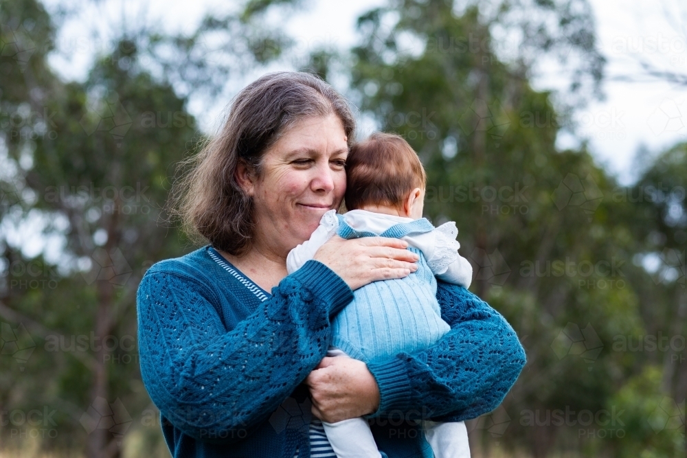 Grandmother smiling while holding and comforting grandchild outside - Australian Stock Image