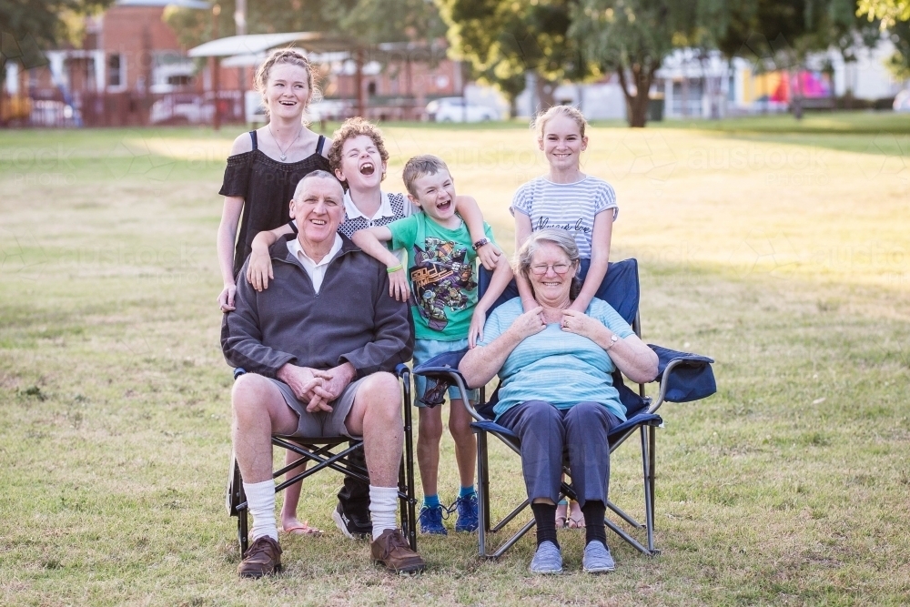 Grandparents sitting on chairs in park laughing with grandchildren - Australian Stock Image
