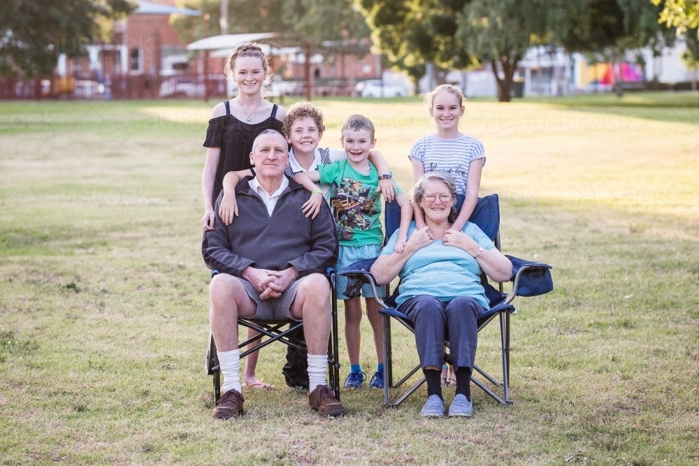 Grandparents sitting on chairs in park with grandchildren - Australian Stock Image