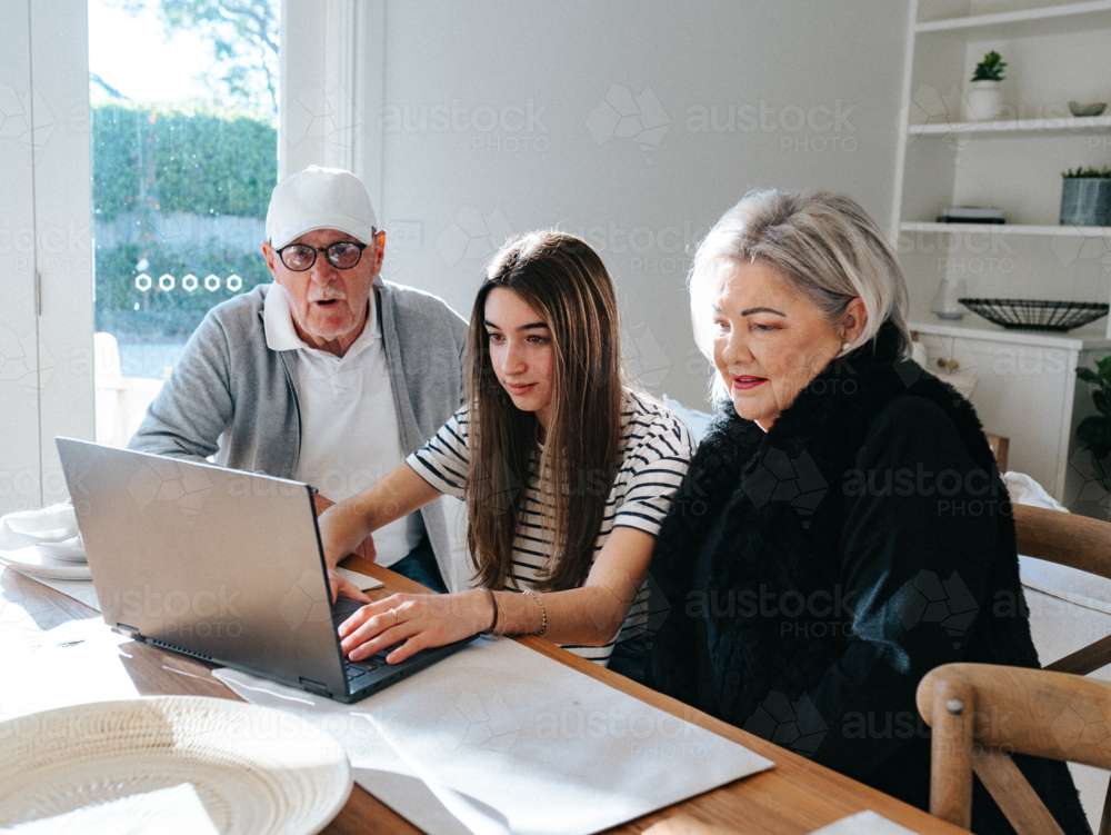 Grandparents sitting with their granddaughter in front of a laptop on the table. - Australian Stock Image