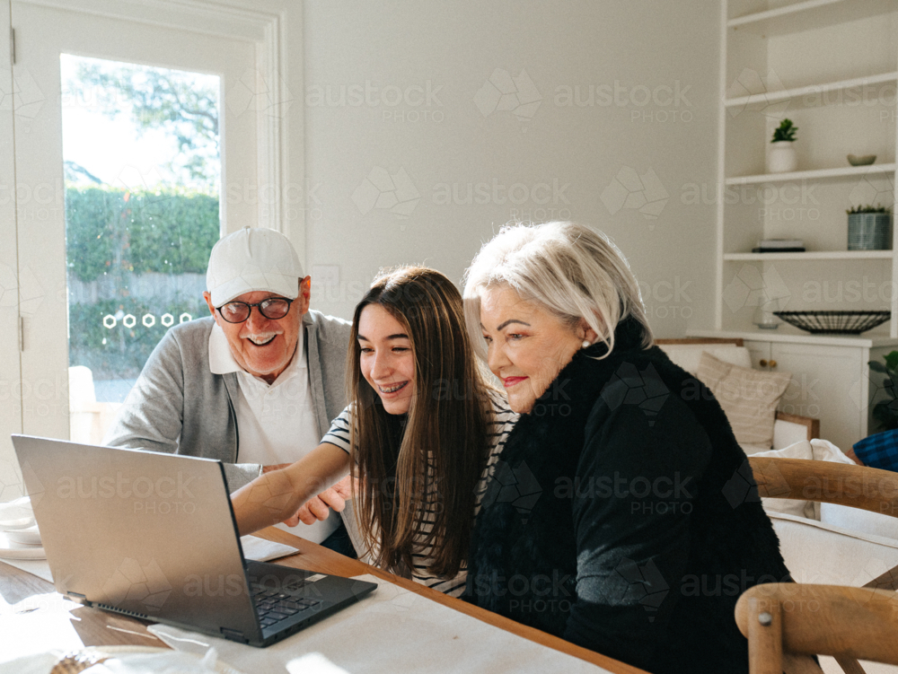 Grandparents sitting with their granddaughter in front of a laptop on the table. - Australian Stock Image