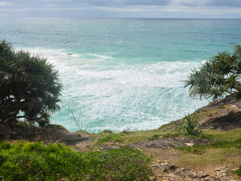 Grass hill down to light blue ocean waves - Australian Stock Image