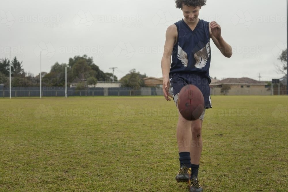 Grassroots Footy player kicking football - Australian Stock Image