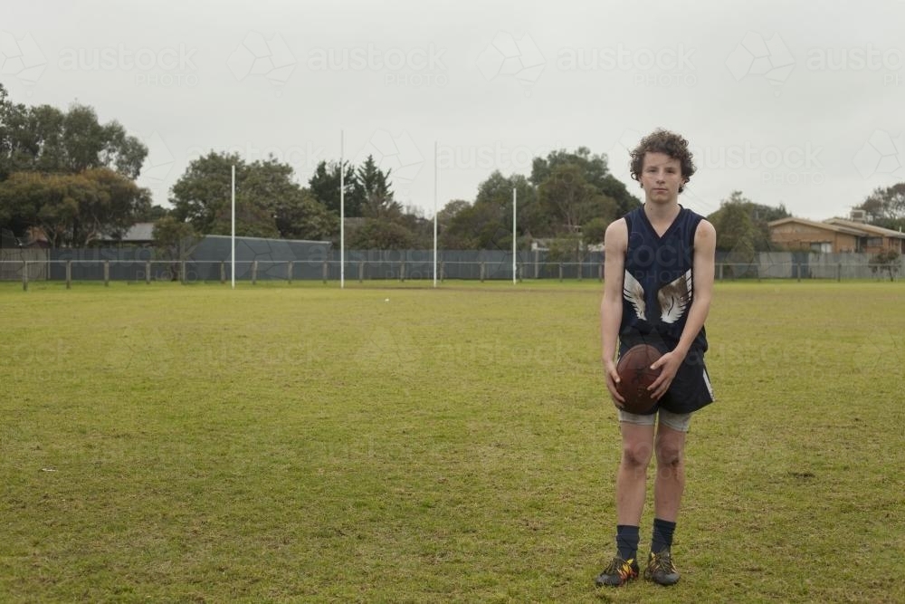 Grassroots Footy player standing with ball on local football ground - Australian Stock Image