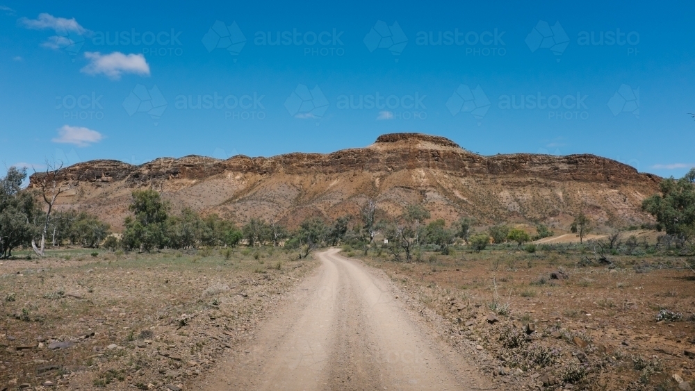 Gravel road leading towards imposing rock formation in the outback - Australian Stock Image