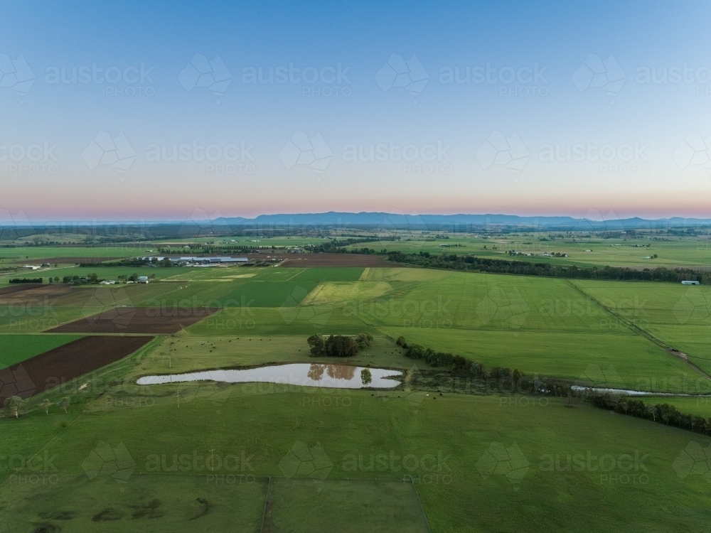 Green farmland landscape at dusk with dam seen from aerial view - Australian Stock Image