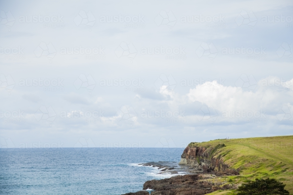 Green hills and cliffs beside flat ocean on overcast day - Australian Stock Image