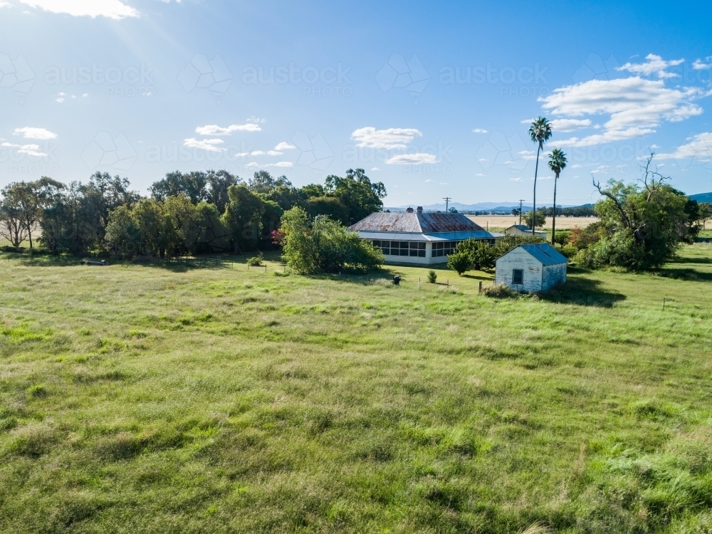 Green paddock with old farm homestead and house yard - Australian Stock Image