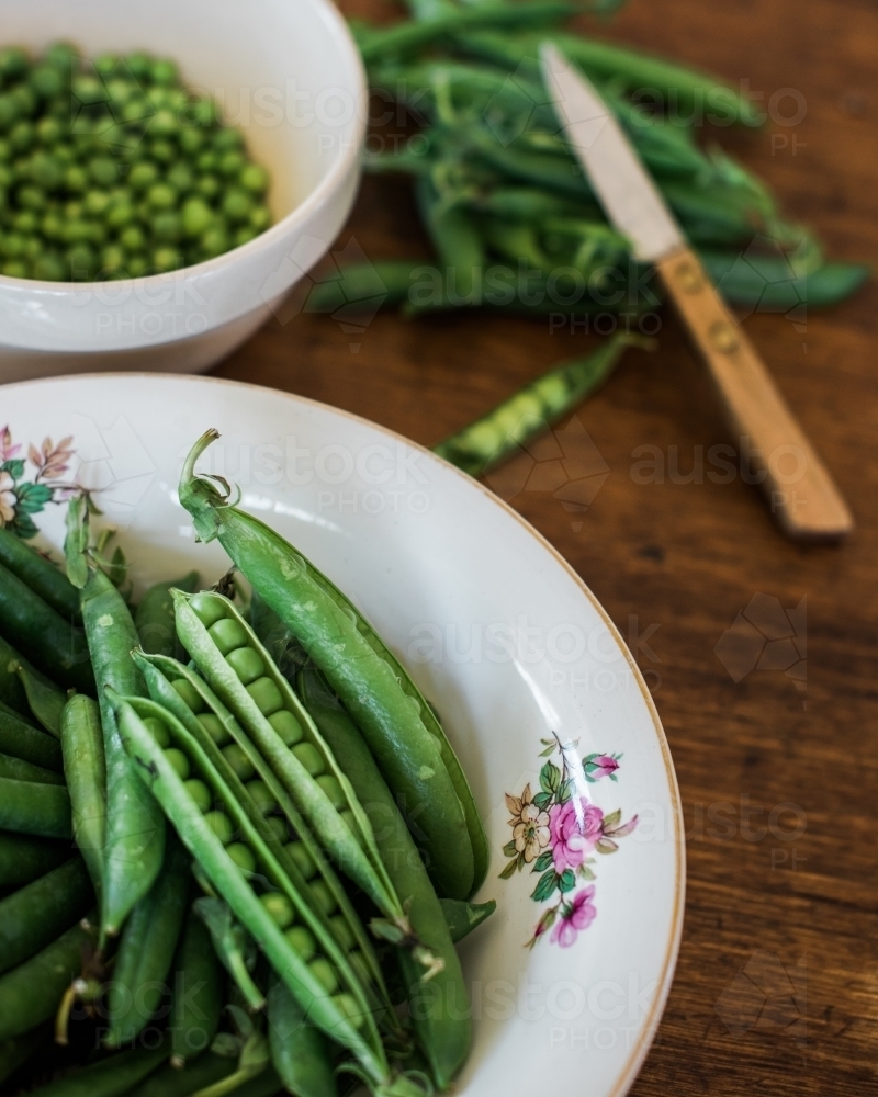 Green pea pods in bowl on table - Australian Stock Image