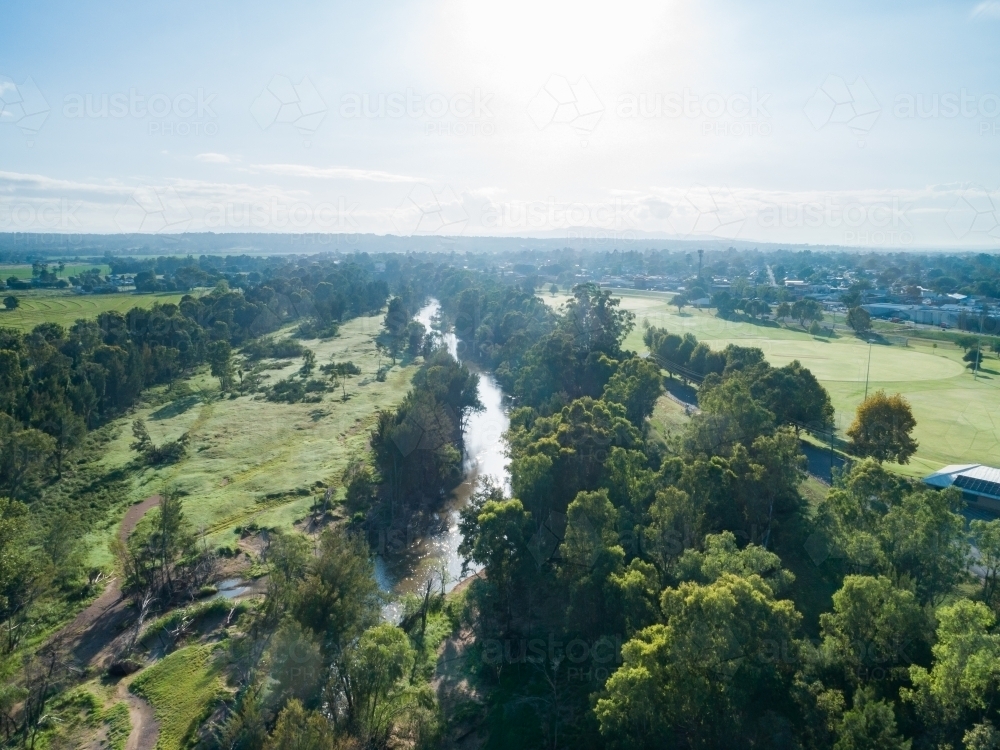 Green riverside grass sparkling from dew in morning light with sun shining on river water - Australian Stock Image