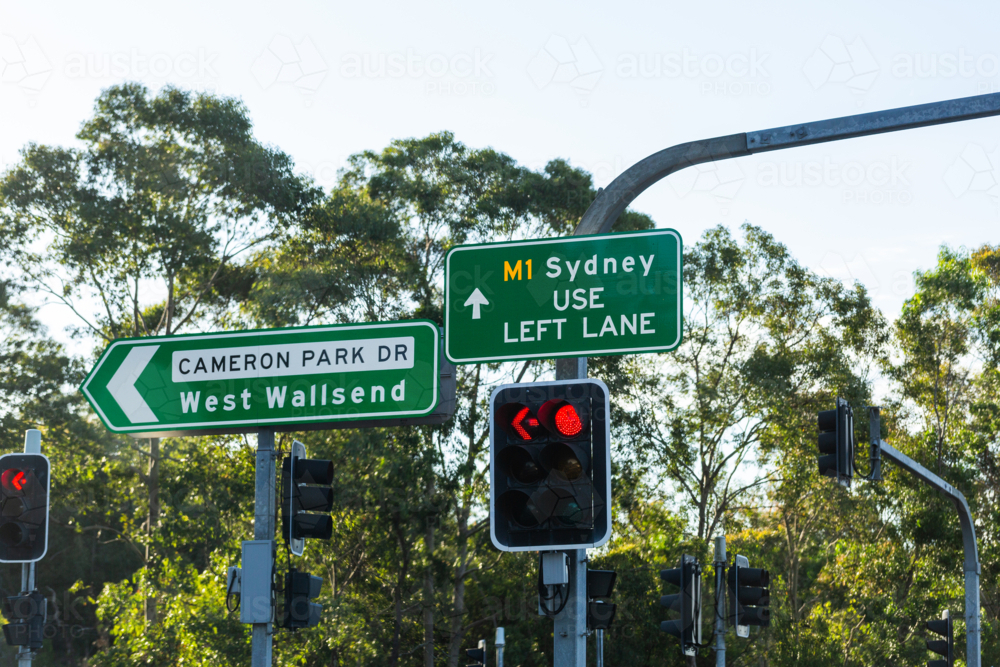 Green road sign to west wallsend on red traffic light pole with signage to Sydney via M1 - Australian Stock Image