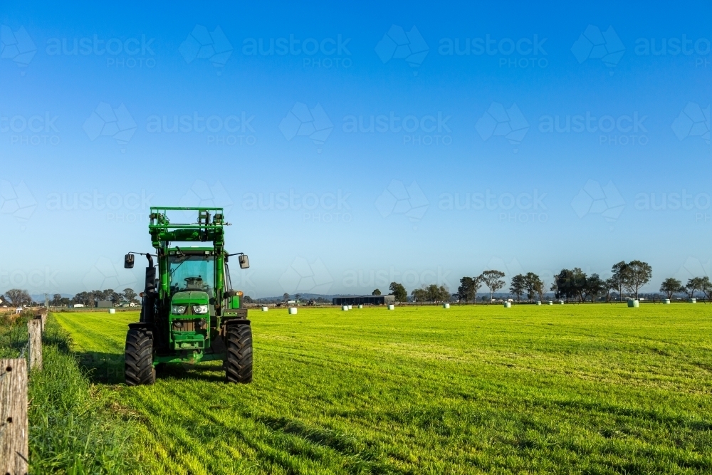 Green tractor in paddock on farm under blue morning sky - Australian Stock Image