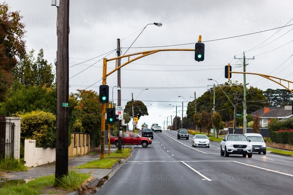 Green Victorian traffic light with cars traveling down road in Melbourne - Australian Stock Image
