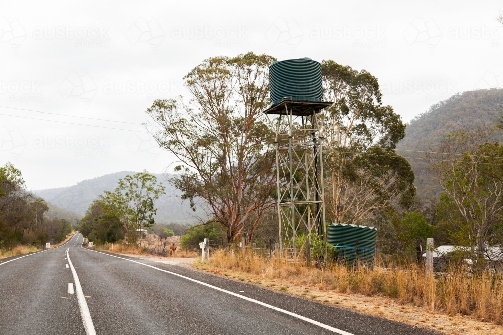 Green water tank on a stand on farm beside road - Australian Stock Image