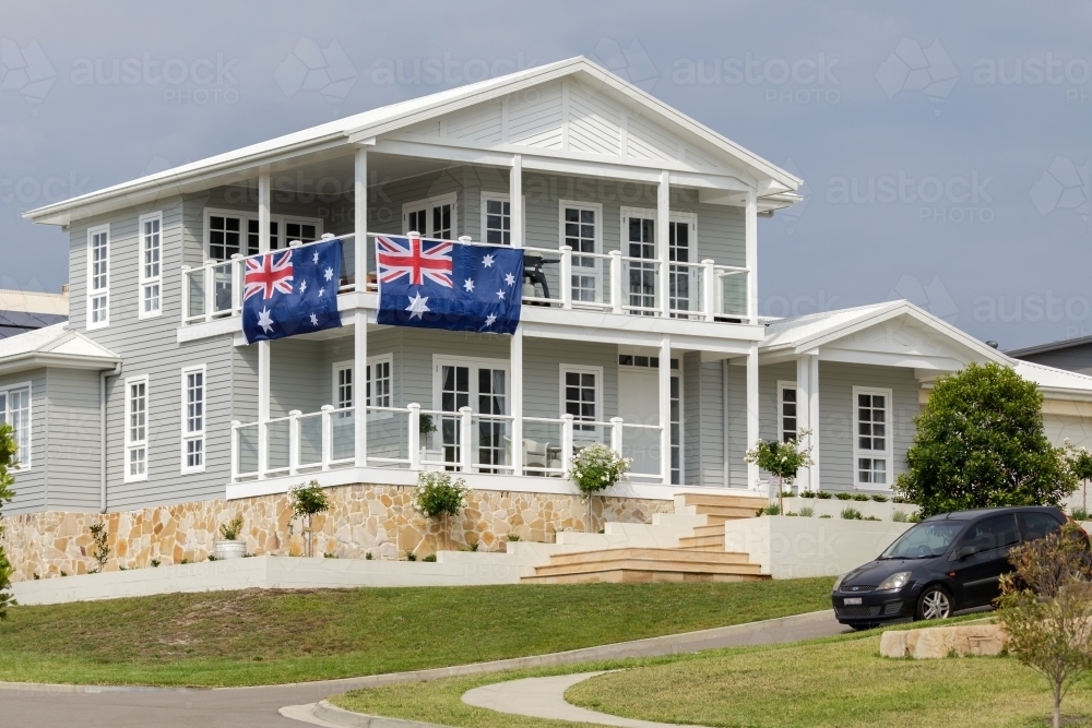 Grey and white Hamptons style house with two large Australian flags hanging from railings - Australian Stock Image