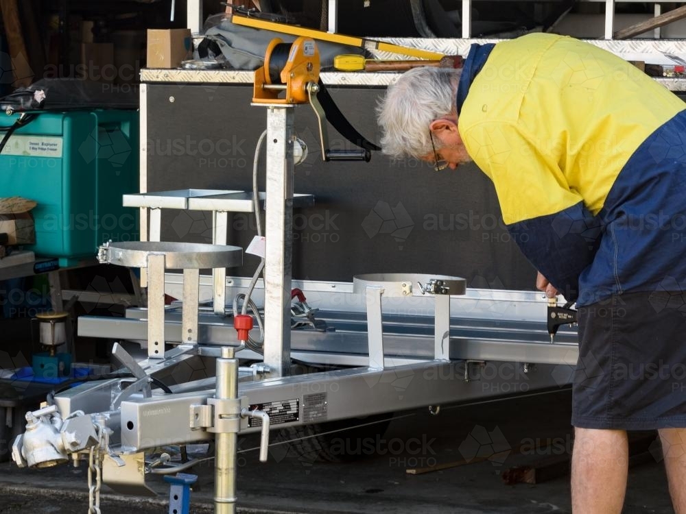 Grey haired man working on drawbar of camper trailer - Australian Stock Image
