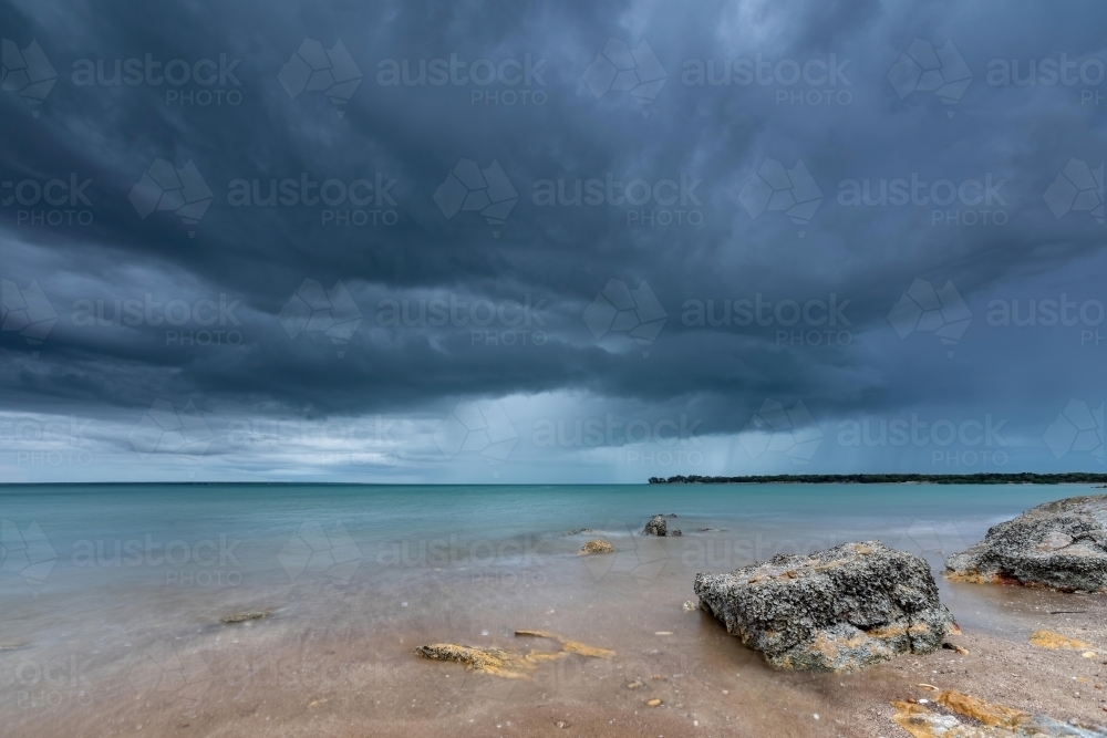 Grey storm clouds overhead with rain falling in the distance over the ocean - Australian Stock Image