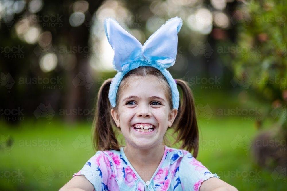 Grinning little girl with Easter bunny ears outside - Australian Stock Image