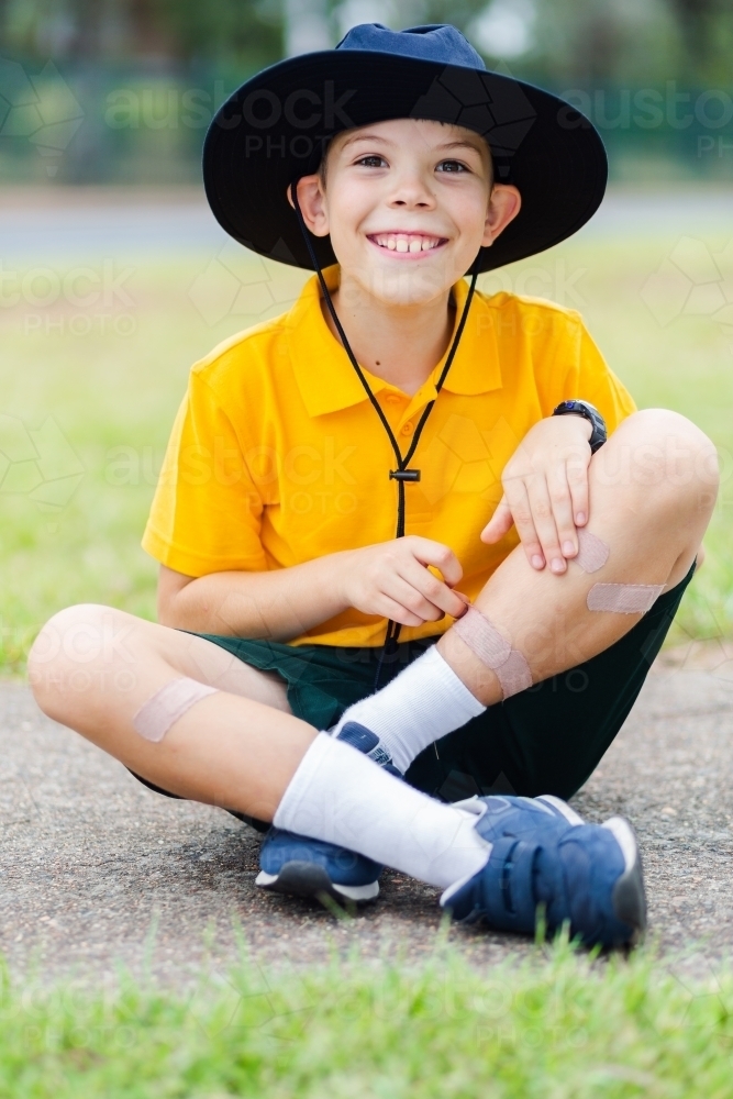 Grinning school kid showing off his band aids covering scrapes on his legs - Australian Stock Image