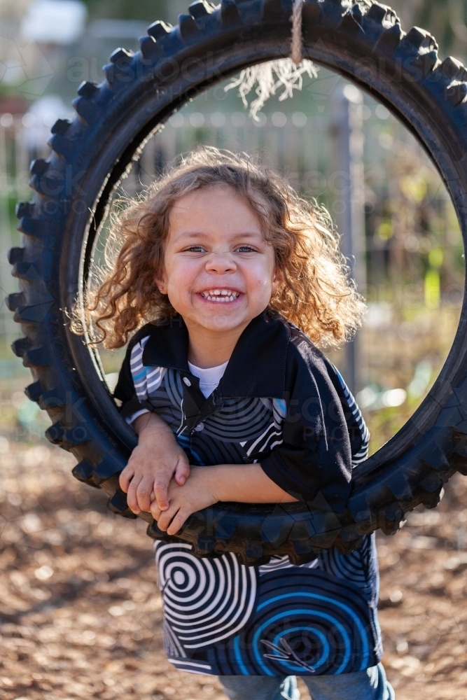 Grinning young aboriginal girl in tyre swing in backyard - Australian Stock Image