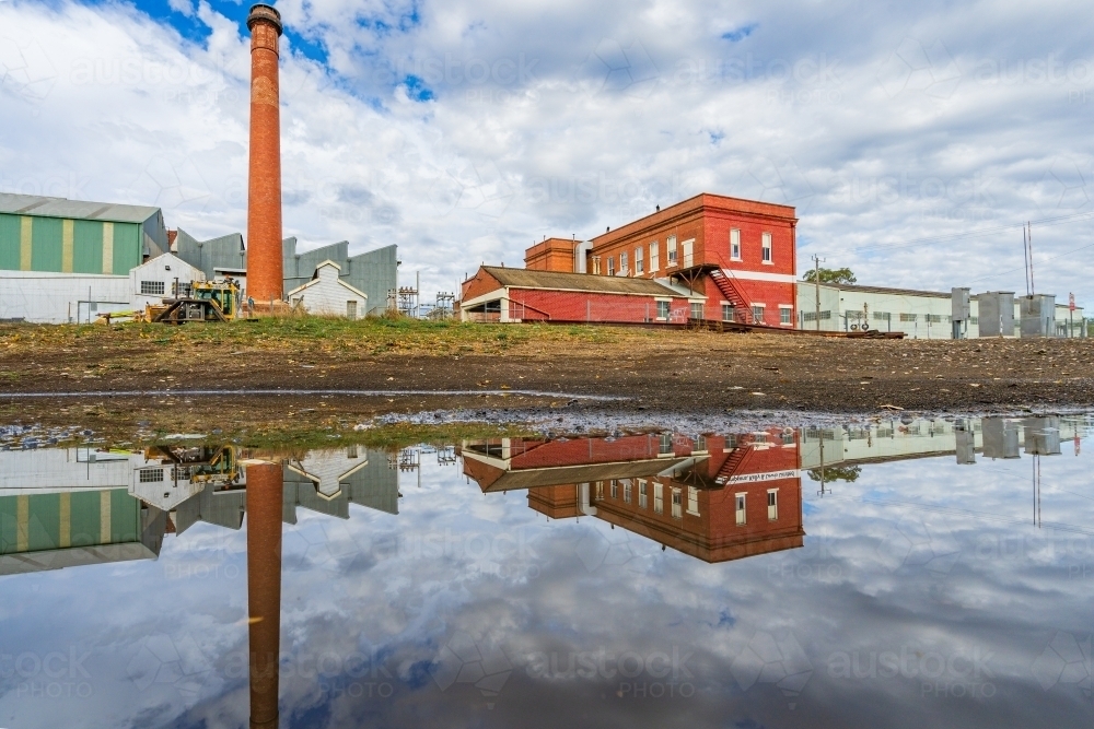 Ground level view of a brick chimney at a  factory and its reflection in a puddle - Australian Stock Image