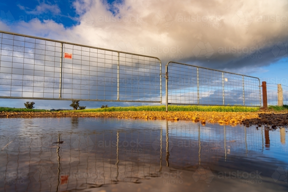Ground level view of a pool of water in front of a farm gate with dramatic clouds above - Australian Stock Image
