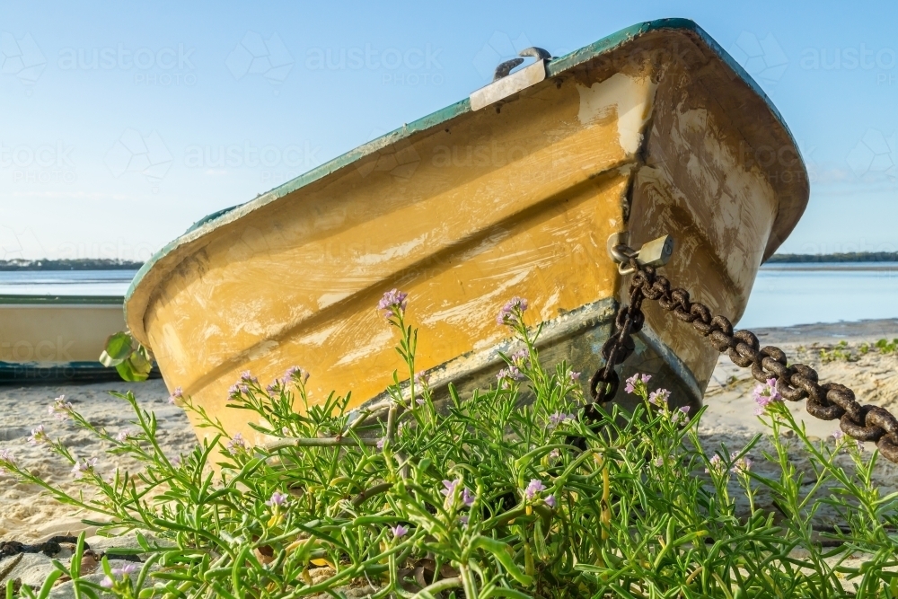 Ground level view of an old row boat chained up on the beach - Australian Stock Image