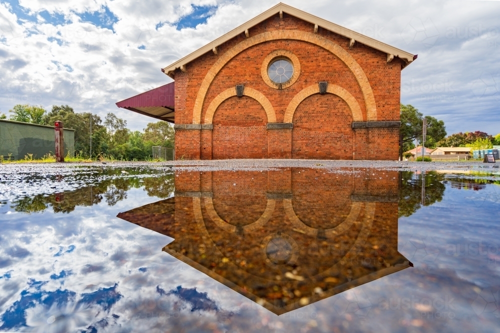 Ground level view of ornate brickwork on goods shed and its reflection in a puddle - Australian Stock Image