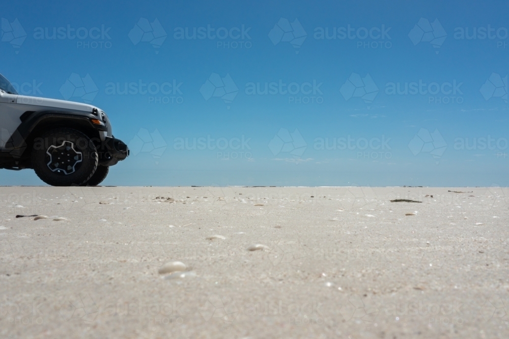 ground level view of white sand looking over to the front section of a 4x4 truck on the beach - Australian Stock Image