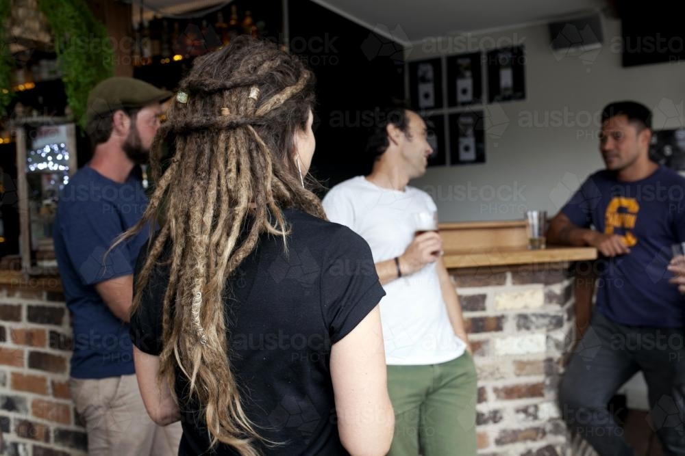 Group of friends catching up at local pub with dreadlocks in foreground - Australian Stock Image