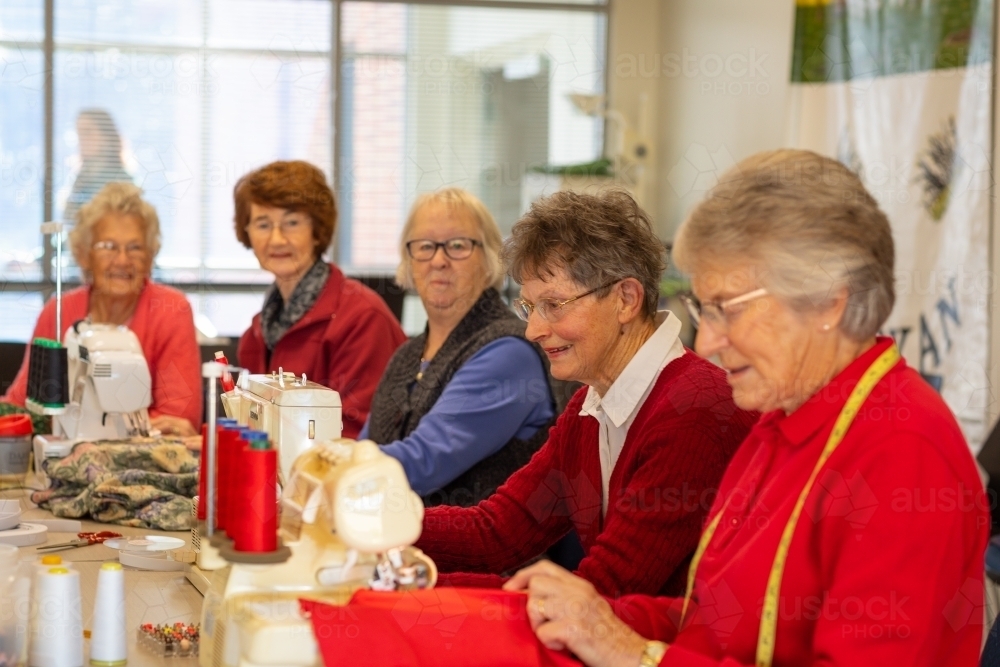 Image of group of ladies sitting around table sewing - Austockphoto