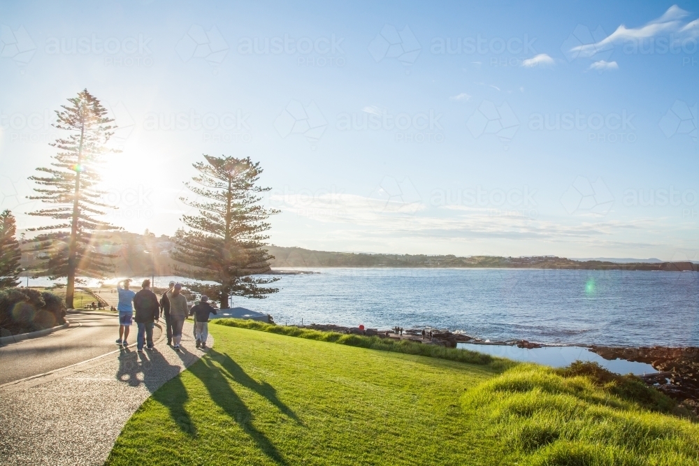 Group of people walking along the coast beside green grass sloping to the sea - Australian Stock Image