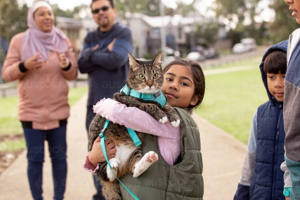 Group of people with a girl wearing green coat holding a cat with blue green leash - Australian Stock Image