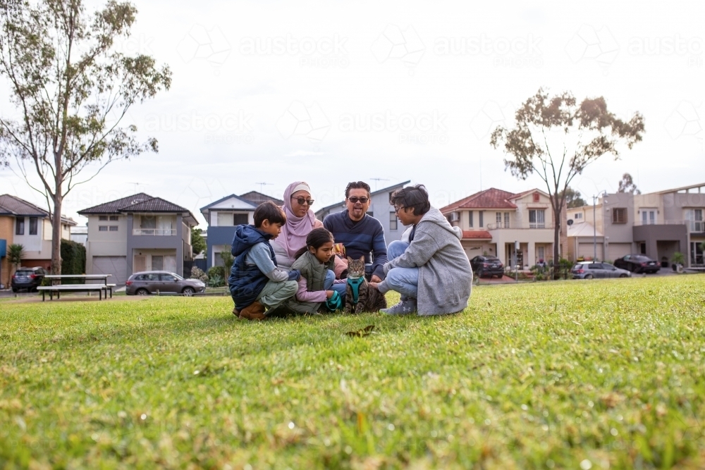Group of people with man woman three children and a cat sitting down on a big lawn - Australian Stock Image