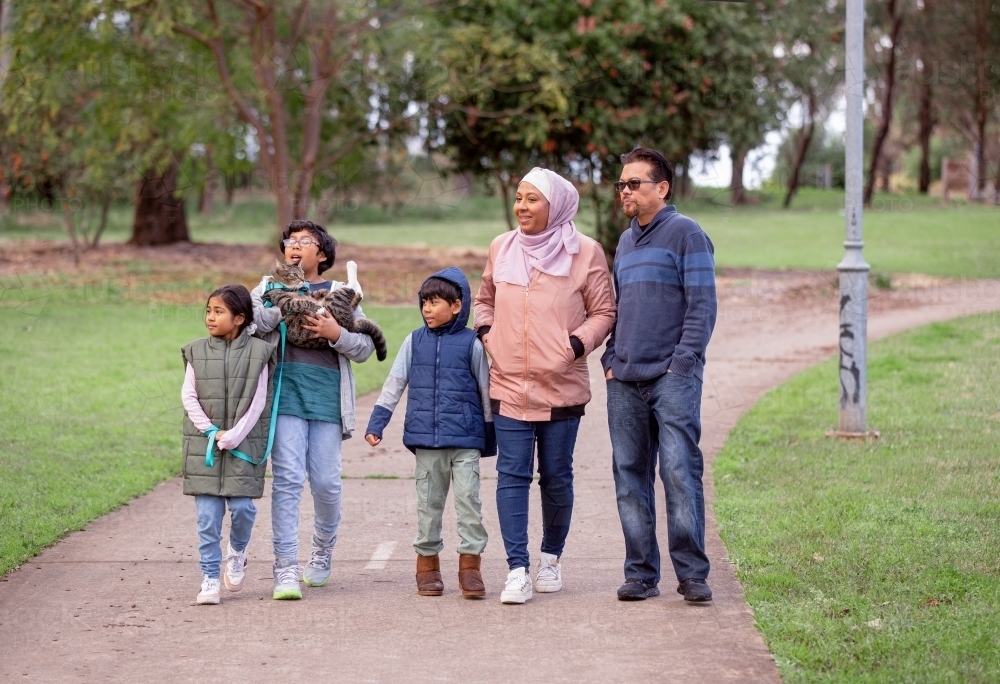 Group of people with one woman wearing pink hijab and a middle aged man three children and a cat - Australian Stock Image