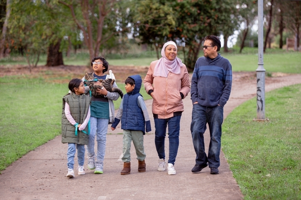 Group of people with one woman wearing pink hijab and a middle aged man three children and a cat - Australian Stock Image