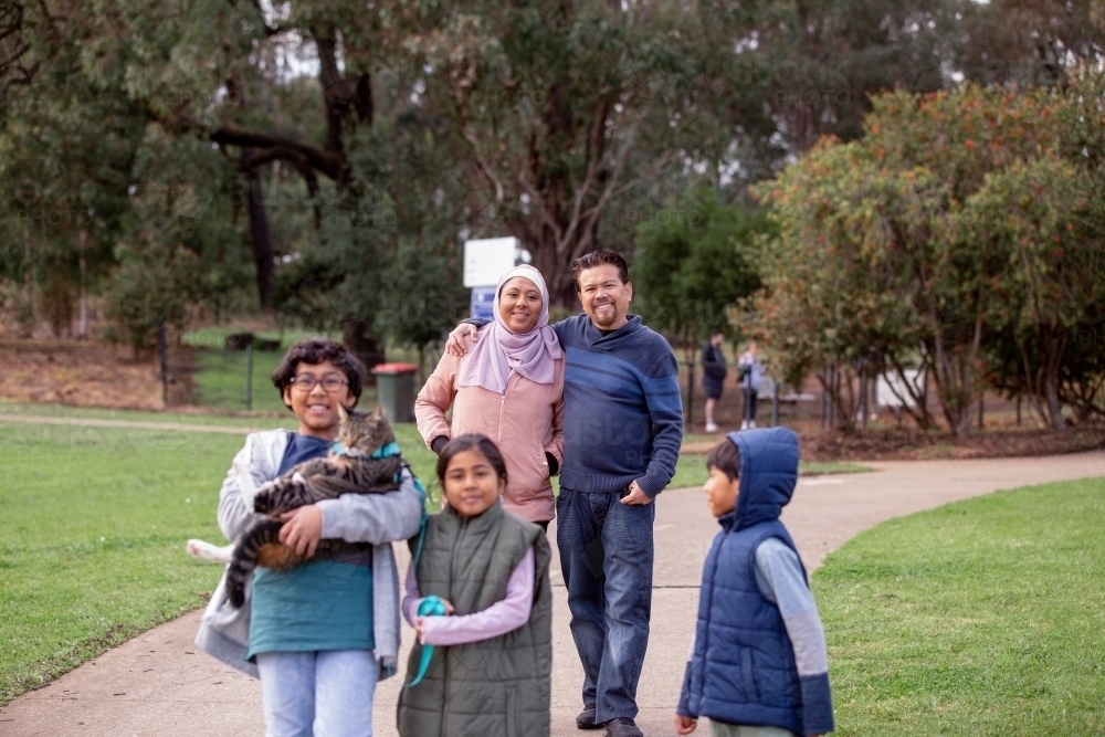 Group of people with one woman wearing pink hijab and a middle aged man three children and a cat - Australian Stock Image