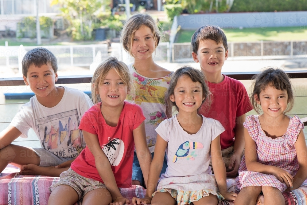 Group of six diverse culture Australian children smiling while sitting close together. - Australian Stock Image